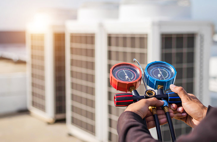 An HVAC technician checking an outdoor AC unit with gauges for Airtechservicesohio.com in Columbus, OH