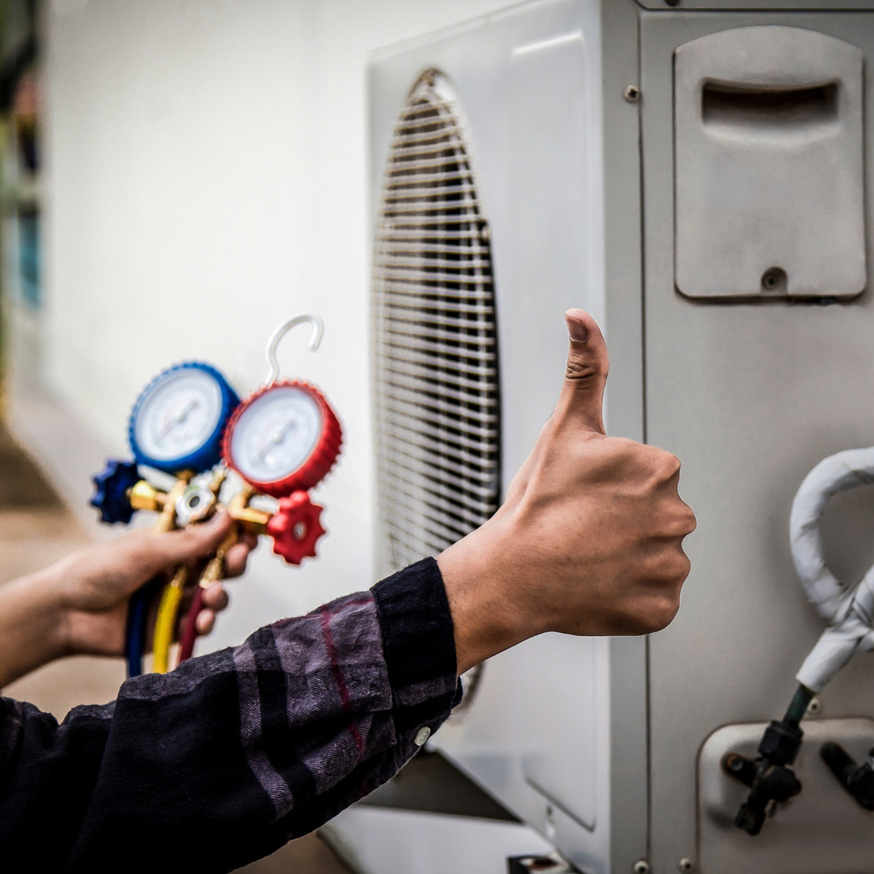 An HVAC technician giving a thumbs-up while checking an AC unit with gauges for M Heating & Cooling, Inc. in Green Bay, WI