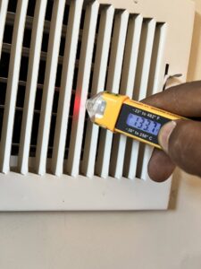An HVAC technician checking the air temperature from a vent with a voltage tester at Keith HVAC & Electrical Enterprises LLC in New Orleans, LA.