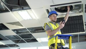 An HVAC technician on a ladder performing maintenance on an overhead commercial HVAC unit for Energy Logix in Austin, TX.