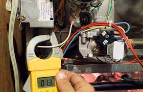 An HVAC technician checking furnace wiring with a clamp meter at AC Service Tech Inc in Cedar Rapids, IA.