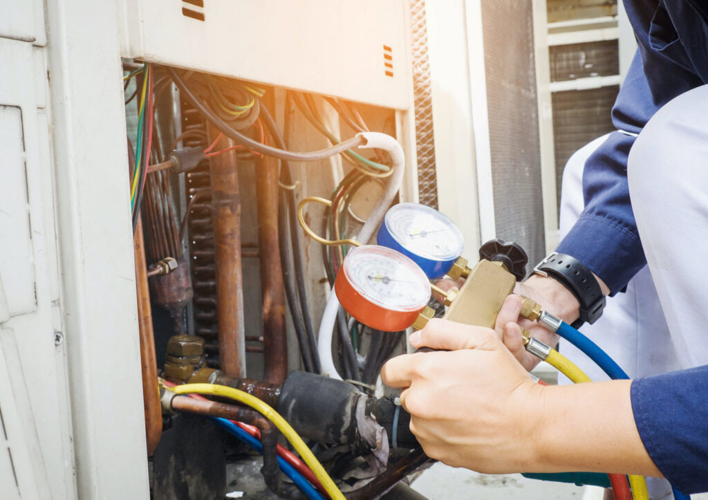 An HVAC technician checking refrigerant levels on an outdoor unit with manifold gauges for Air Works of Alabama LLC in Mobile, AL.