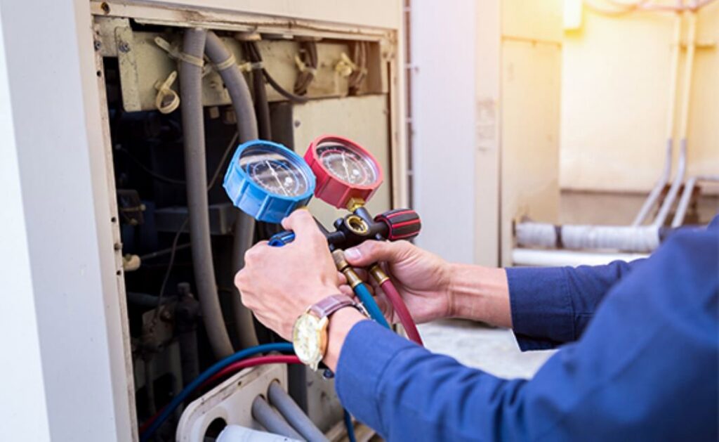An HVAC technician checking refrigerant levels on an outdoor unit with gauges for J & J Heating and Cooling, Inc. in Lancaster, PA.