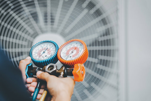 An HVAC technician checking refrigerant pressure with manifold gauges on an outdoor AC unit for Reed's Heating & Cooling in Toms River, NJ.