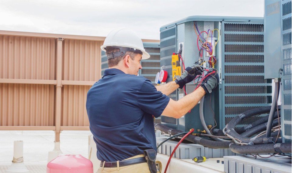 HVAC technician checking refrigerant pressure with manifold gauges on an outdoor AC unit by Taylor & Tyler HVAC, New Orleans, LA.