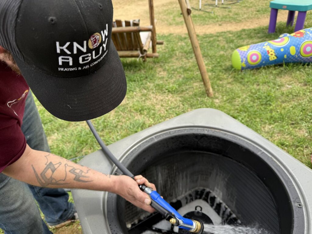 An HVAC technician cleaning the condenser coils of an outdoor air conditioning unit for Know A Guy Heating & Air Conditioning in Kernersville, NC.