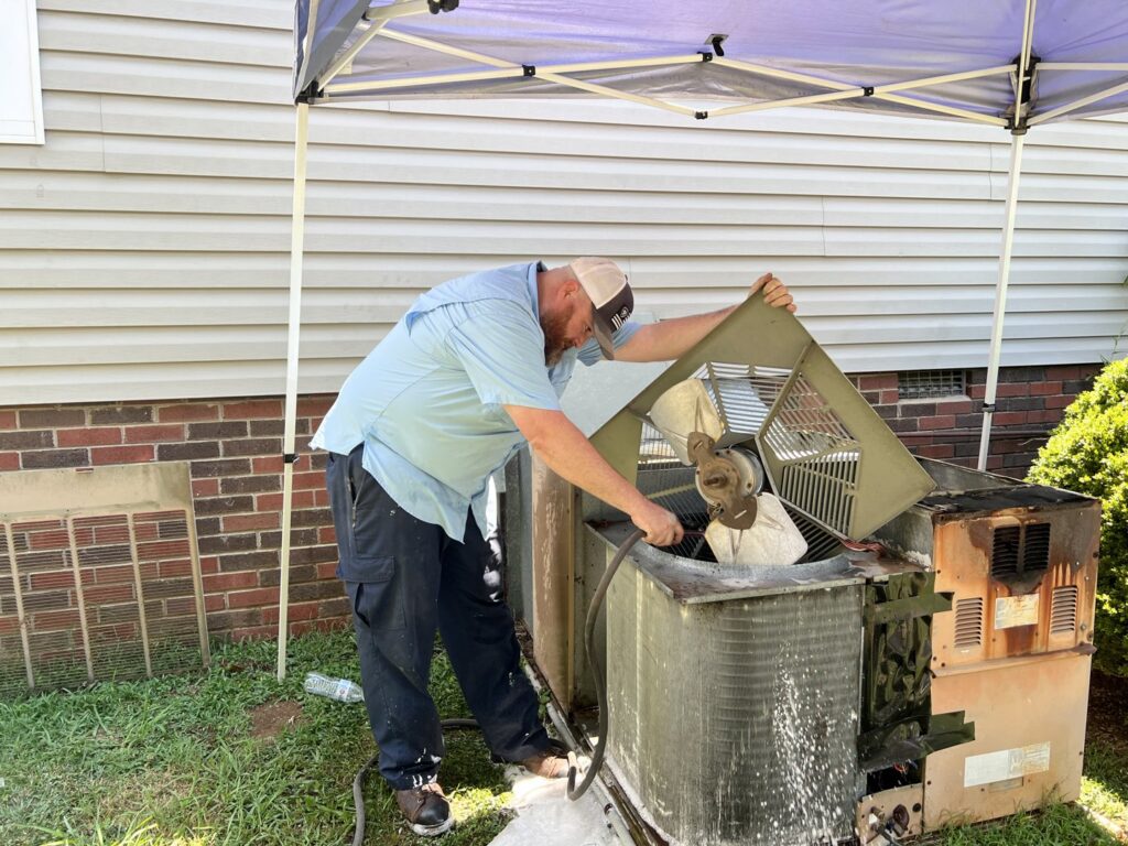 An HVAC technician cleaning an outdoor air conditioning condenser unit for Workman Mechanical in Graham, NC.