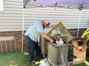 An HVAC technician cleaning an outdoor air conditioning condenser unit for Workman Mechanical in Graham, NC.