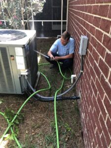 An HVAC technician cleaning an outdoor air conditioning unit at a home in Sumter, SC for Advance Heating & Air, Inc.