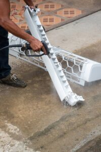 An HVAC technician cleaning an air conditioning unit component with a pressure washer for General Air Conditioning Service Corp in Greenville, SC.