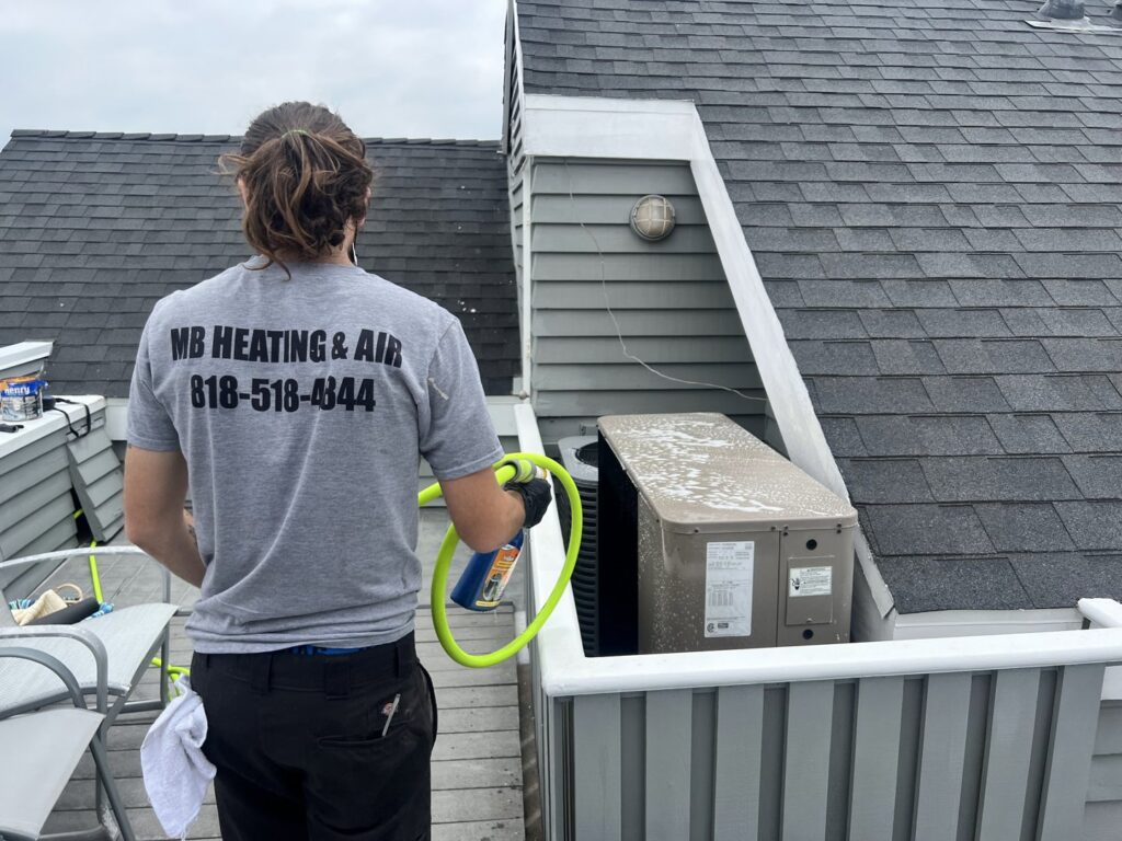 An MB Heating and Air technician cleaning an outdoor AC unit during a service call in Northridge, CA.
