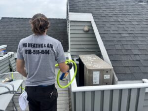 An MB Heating and Air technician cleaning an outdoor AC unit during a service call in Northridge, CA.