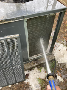 An HVAC technician cleaning an outdoor AC unit with a hose at a client's home by Your Angel Heating And Cooling LLC in Cary, NC.