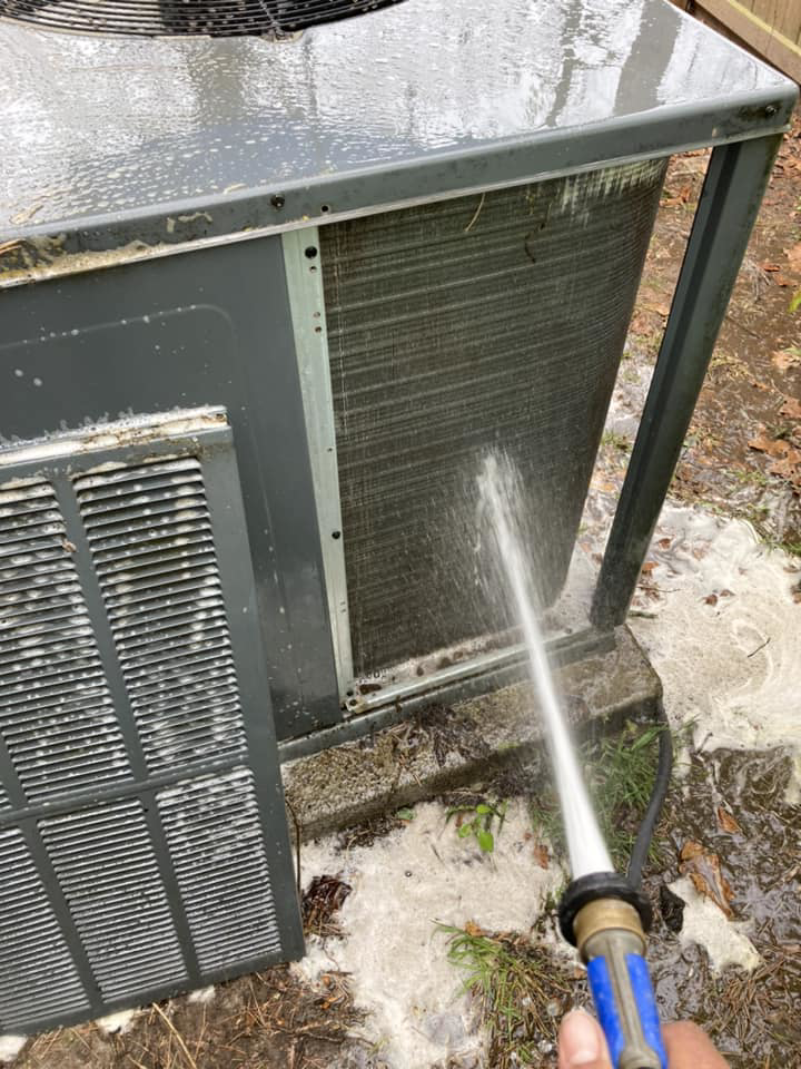 An HVAC technician cleaning an outdoor AC unit with a hose at a client's home by Your Angel Heating And Cooling LLC in Cary, NC.