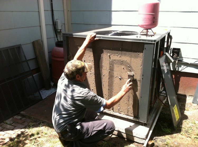 An HVAC technician cleaning a dirty outdoor condenser unit for R A Styron Heating & Air Conditioning, Inc. in Chesapeake, VA.