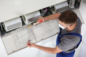 An HVAC technician wearing a mask cleaning an indoor air conditioning unit at ABE HVAC in Novi, MI.