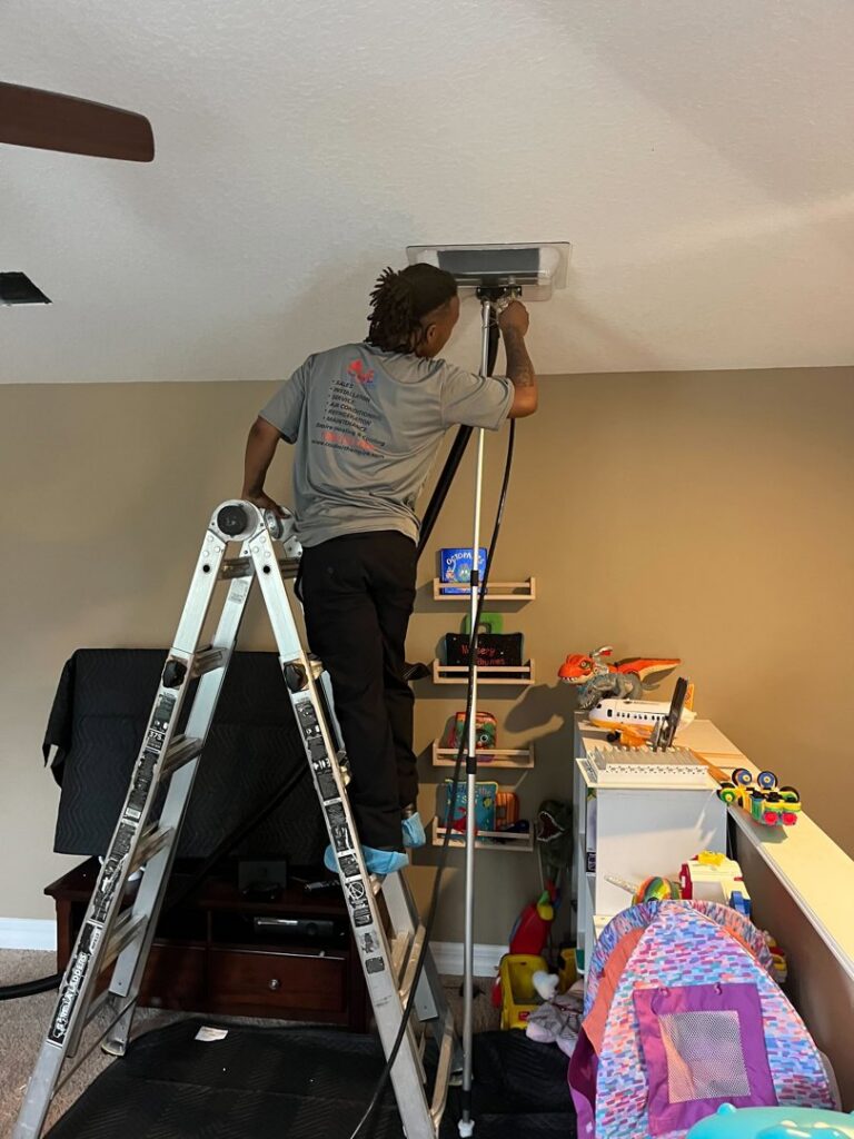 An HVAC technician on a ladder cleaning an indoor vent for Timely Air Conditioning in Riverview, FL.