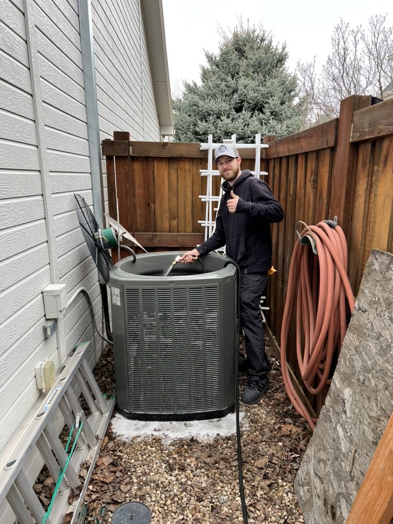 An HVAC technician cleaning an outdoor air conditioning unit for Access Heating & Air Conditioning in Fredericksburg, VA