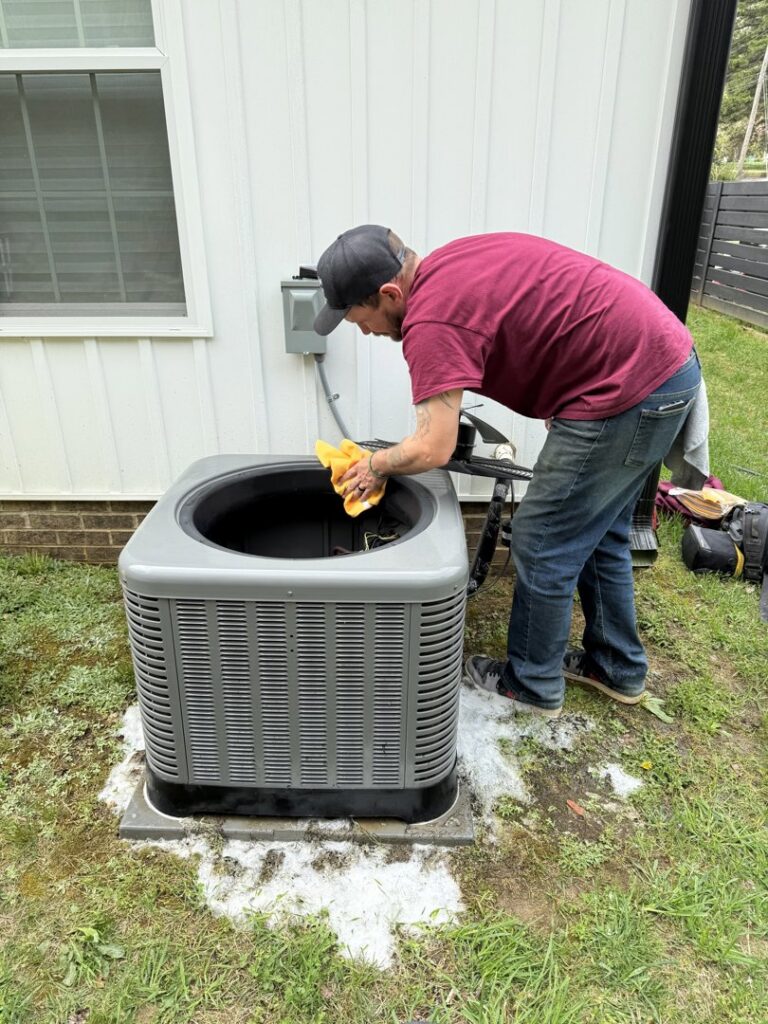 An HVAC technician cleaning an outdoor air conditioning unit for a client of Know A Guy Heating & Air Conditioning in Kernersville, NC.