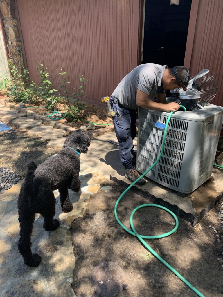 An HVAC technician cleaning an outdoor AC unit during maintenance for OKIE Heating and Cooling in Tulsa, OK.