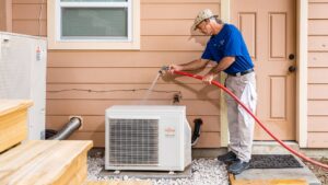 An HVAC technician from Mr. Cool HVAC cleaning an outdoor Fujitsu condenser unit with a hose in Cypress, TX.