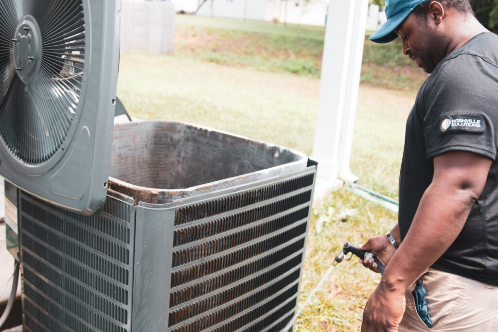 An HVAC technician from Nashville Solutions cleaning an outdoor air conditioning unit in Nashville, TN