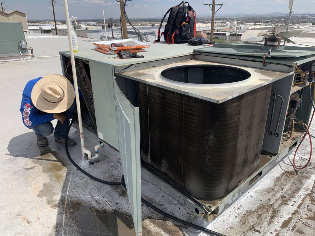 An HVAC technician cleaning the coils of a rooftop air conditioning unit by EA Heating & Cooling in El Paso, TX.