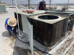 An HVAC technician cleaning the coils of a rooftop air conditioning unit by EA Heating & Cooling in El Paso, TX.