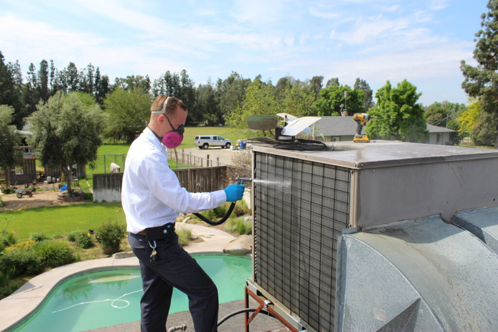 An HVAC technician cleaning a large rooftop air conditioning unit for maintenance by Controlled Climates Heating and Air Conditioning, Inc. in Fresno, CA.