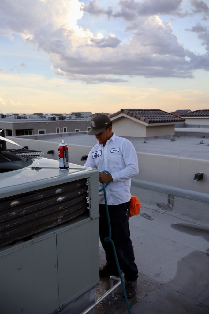 An Ignitify Commercial Grade HVAC technician cleaning a rooftop HVAC unit coil with a hose and spray in El Paso, TX.