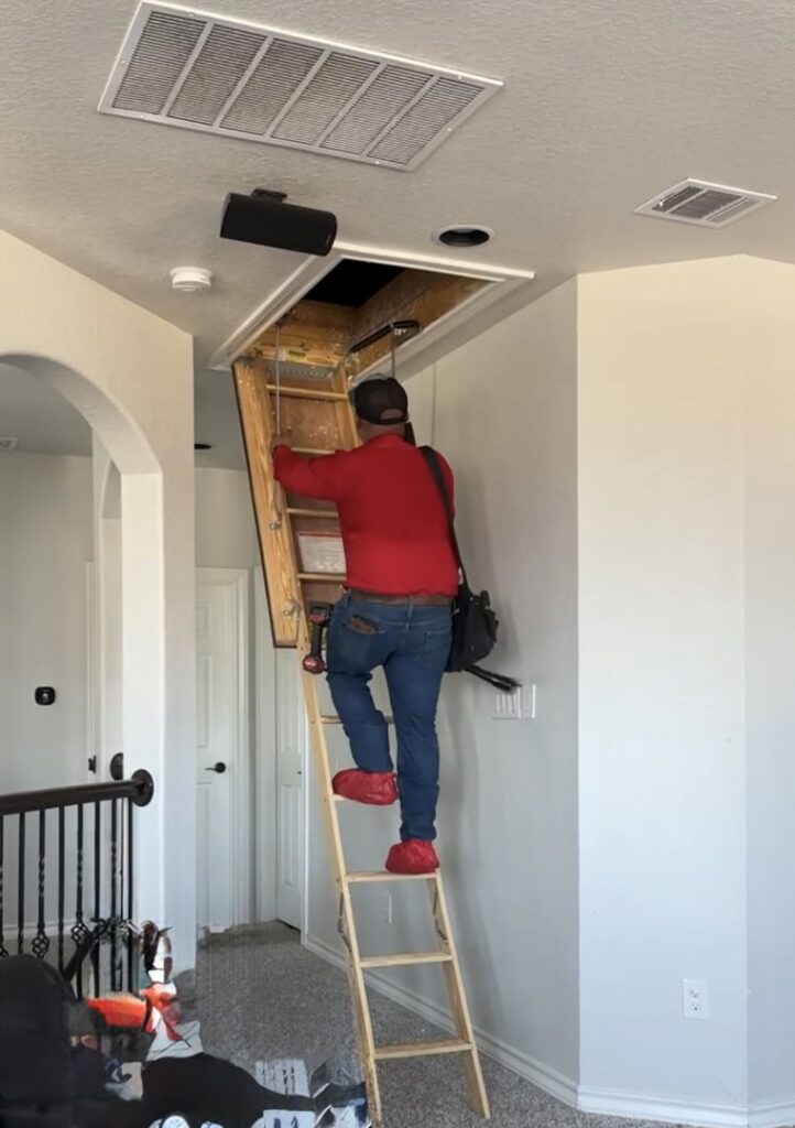 An HVAC technician from Manuel & Sons Service Co. climbing an attic ladder for service in San Antonio, TX.
