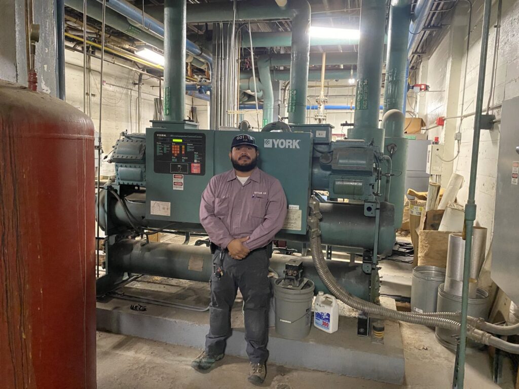 An HVAC technician standing in front of large commercial chillers at a facility serviced by Gotham Air LLC in Glendale, AZ.
