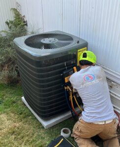 An HVAC technician from JCL Heating and Cooling LLC connecting gauges to an outdoor AC unit in Gresham, OR.