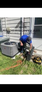 An HVAC technician connecting gauges to an outdoor AC unit for service by Anderson's Air in Newport News, VA