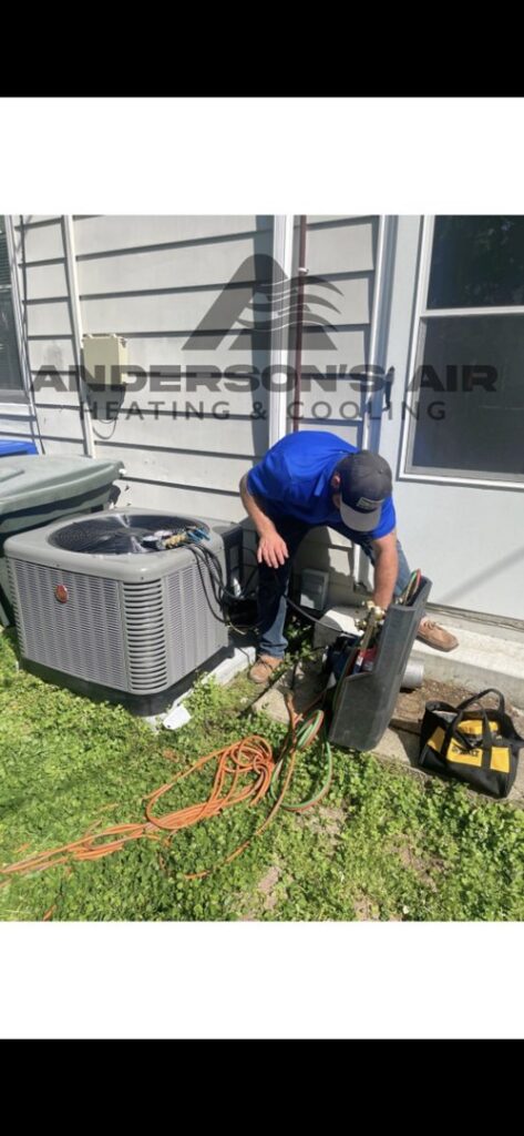 An HVAC technician connecting gauges to an outdoor AC unit for service by Anderson's Air in Newport News, VA