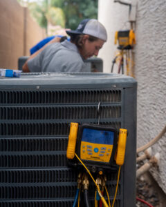 An HVAC technician connecting gauges to an outdoor AC unit for service by Viking Heating and Air Conditioning, LLC in Chandler, AZ