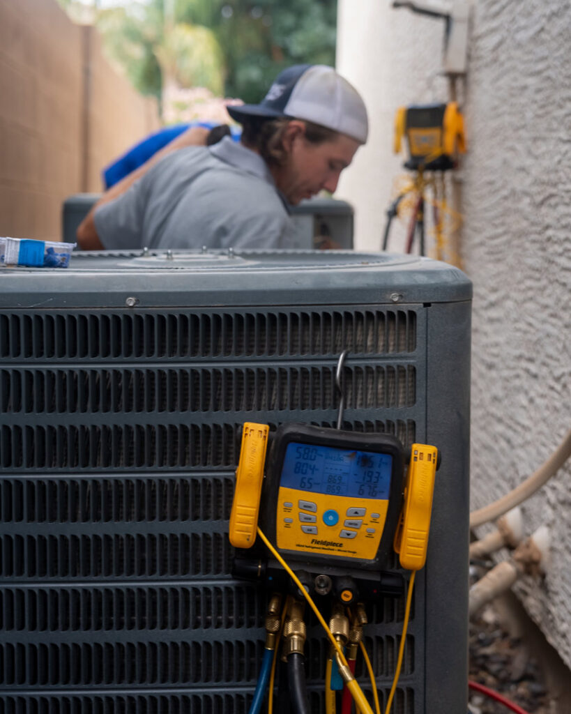 An HVAC technician connecting gauges to an outdoor AC unit for service by Viking Heating and Air Conditioning, LLC in Chandler, AZ