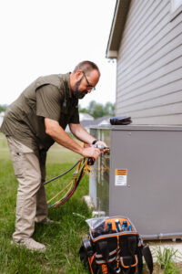 An HVAC technician connecting gauges to an outdoor air conditioning unit for Grace Heating & Air in Clarksville, TN.