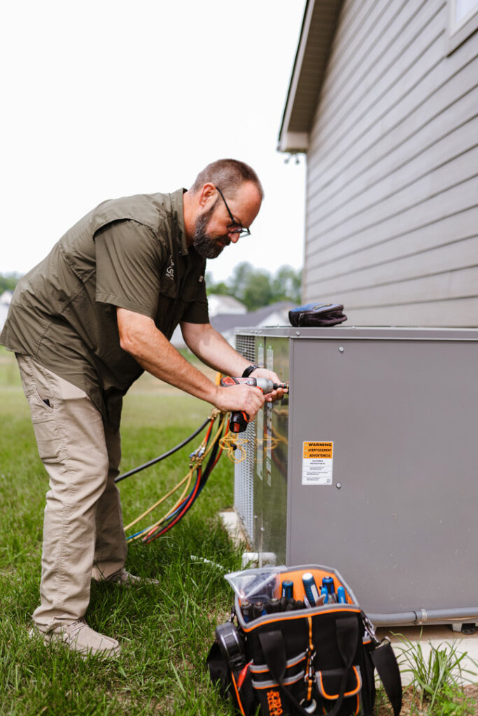 An HVAC technician connecting gauges to an outdoor air conditioning unit for Grace Heating & Air in Clarksville, TN.