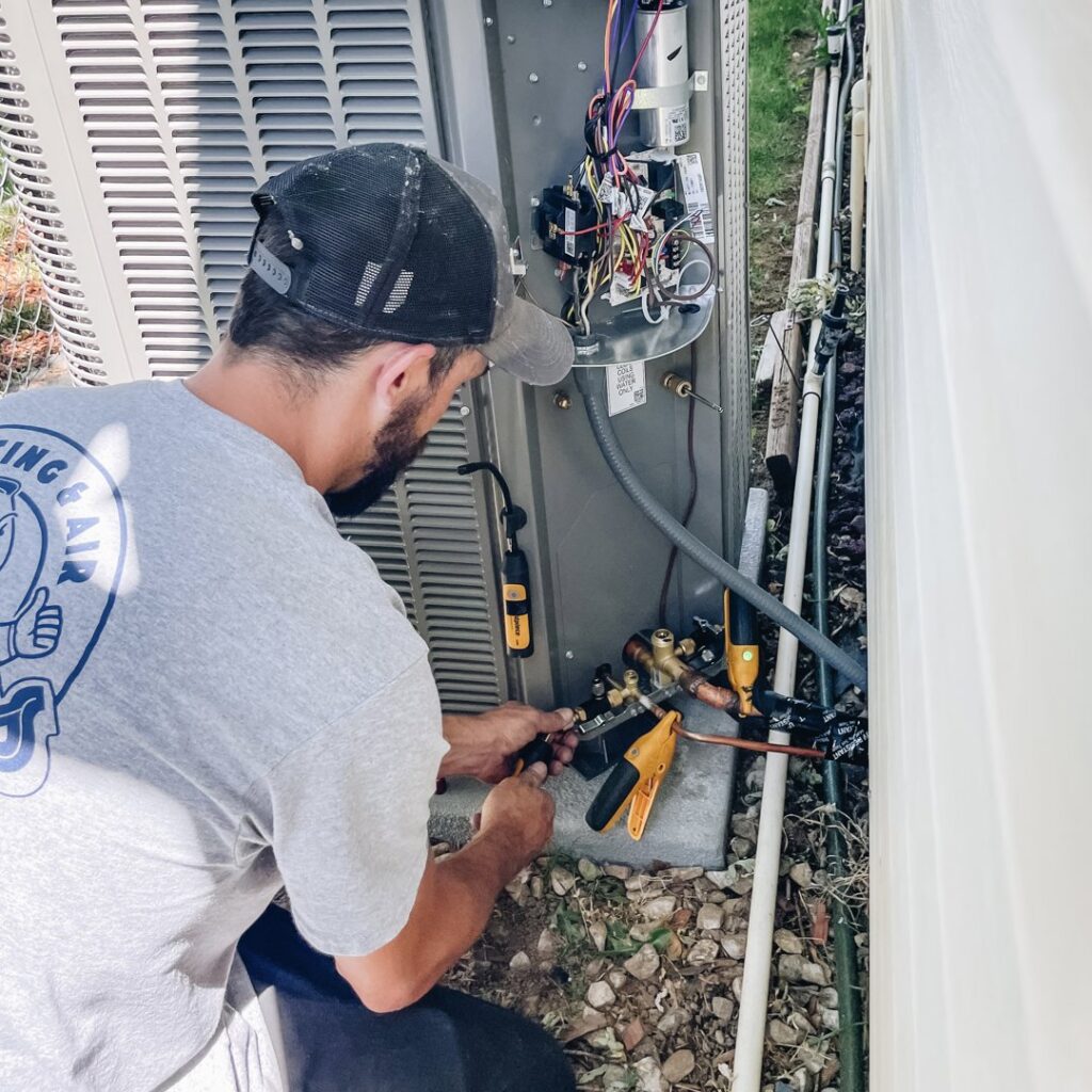An HVAC technician connecting gauges to an outdoor air conditioning unit for service by Access Heating & Air Conditioning in Fredericksburg, VA