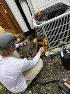 An HVAC technician connecting gauges to an outdoor air conditioning unit for service by Cummings Inc. in Puyallup, WA.