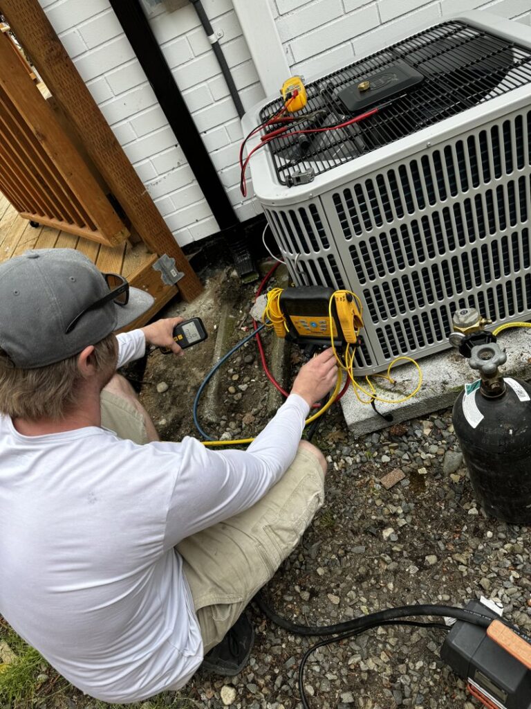 An HVAC technician connecting gauges to an outdoor air conditioning unit for service by Cummings Inc. in Puyallup, WA.