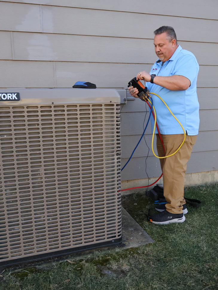 An HVAC technician connecting refrigerant gauges to an outdoor AC unit for Wright Way Air in Streamwood, IL