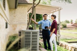 An Aire Serv technician consulting with a customer next to an outdoor AC unit in West Fargo, ND.