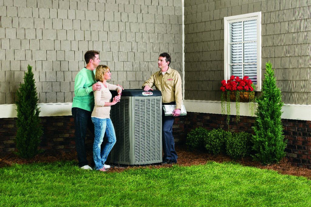 An HVAC technician consulting with customers next to an AC unit for Larry's Heating and Cooling, Inc. in Yankton, SD.