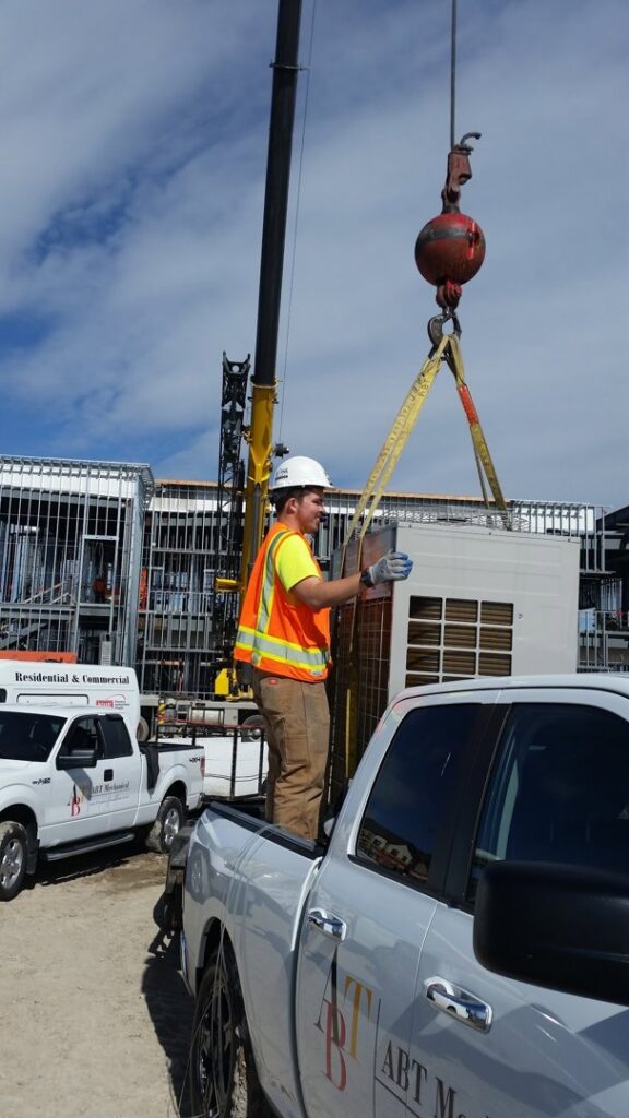 An HVAC technician assisting with a crane installation of a new unit for ABT Heating and Cooling in Orem, UT.