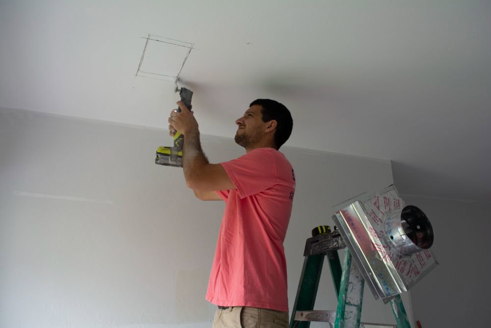 An HVAC technician from Coral Air Conditioning cutting a ceiling opening for a new vent installation in Cape Coral, FL.