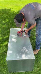 A True Comfort Heating and Cooling technician cutting sheet metal ductwork for an HVAC installation in Sherwood, AR.