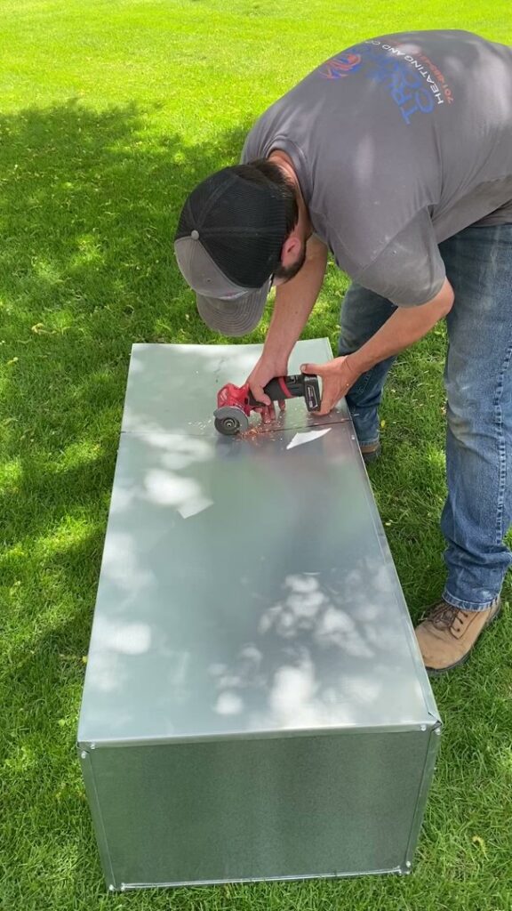 A True Comfort Heating and Cooling technician cutting sheet metal ductwork for an HVAC installation in Sherwood, AR.