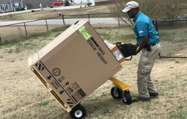 An HVAC technician delivering a new boxed HVAC unit on a dolly to a client's home for Relief Heating and Cooling, LLC in Greensboro, NC.